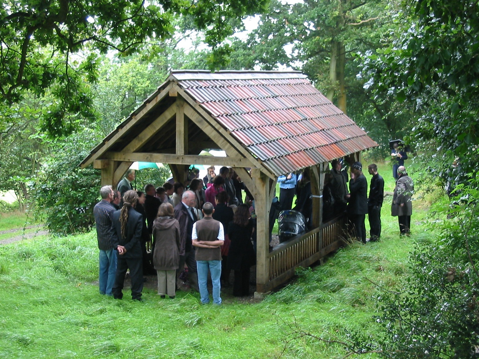 A celebrant led funeral at Usk Castle Chase, with a group of people standing within the memorial shelter.